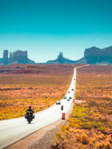 Classic panorama view of motorcyclist on historic U.S. Route 163 running through famous Monument Valley in beautiful golden evening light at sunset in summer, Utah, USA